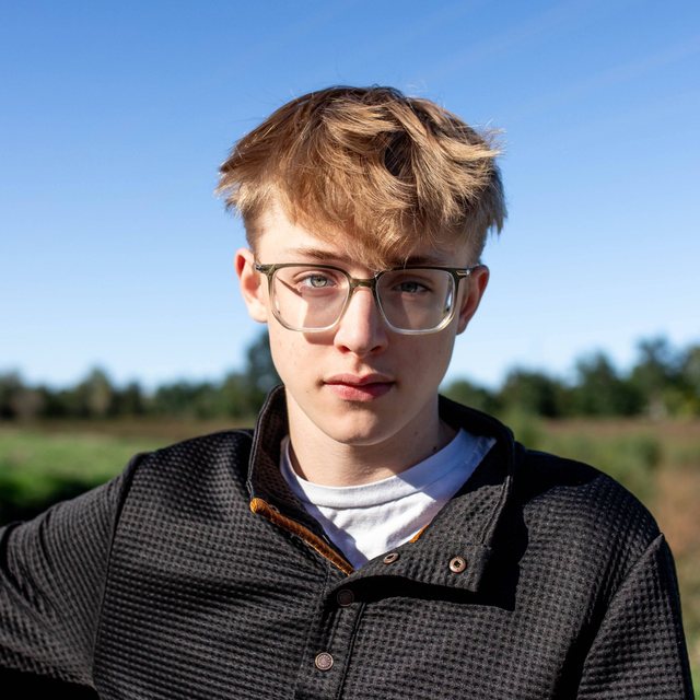 Jack in glasses and a black pullover, outdoors under a blue sky